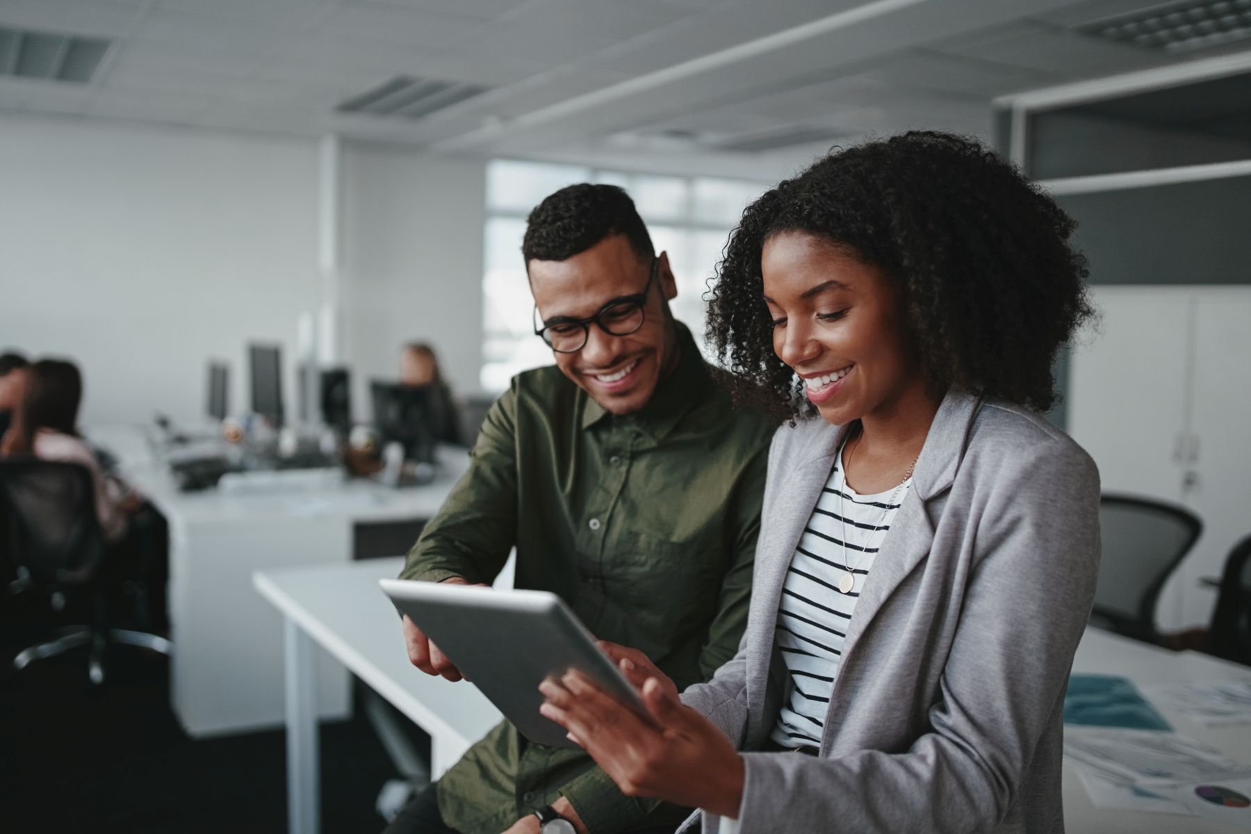 Smiling young african american professional businessman and businesswoman together working online with a digital tablet in office Professional young businesspeople using tablet computer smiling in office
