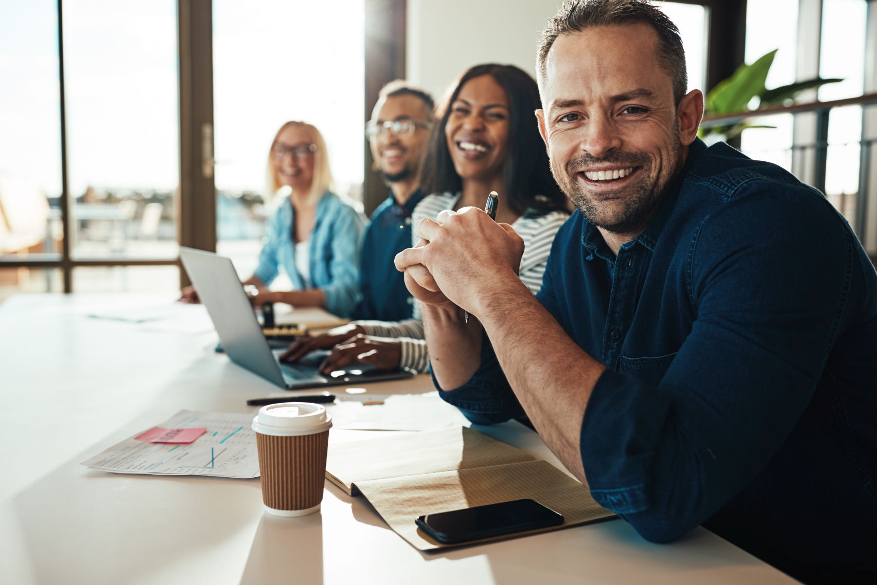Smiling mature businessman sitting with colleagues in an office Smiling businessman sitting with a diverse group of coworkers during a meeting together at a table in an office