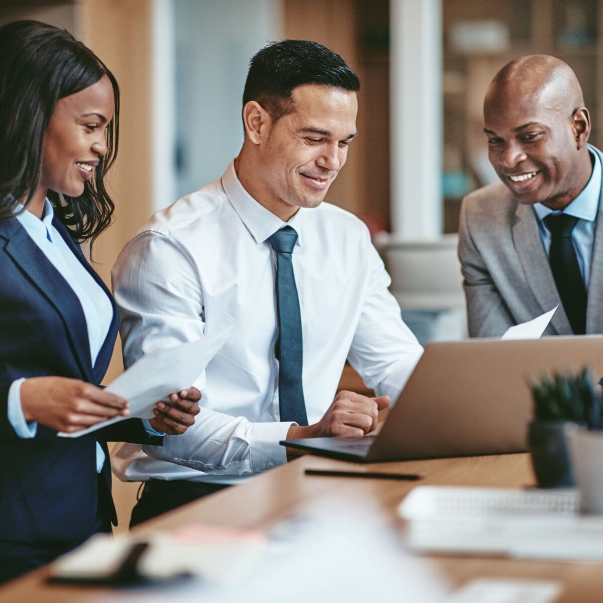 Diverse group of smiling businesspeople working in an office Smiling group of diverse businesspeople going over paperwork together and working on a laptop at a table in an office