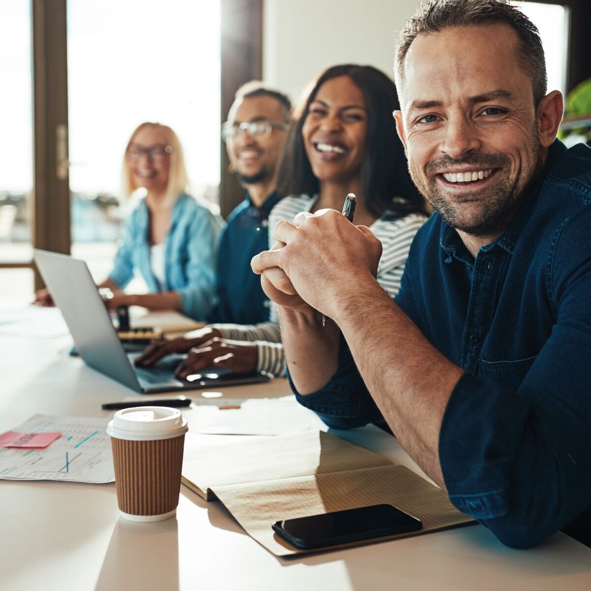 Smiling mature businessman sitting with colleagues in an office Smiling businessman sitting with a diverse group of coworkers during a meeting together at a table in an office